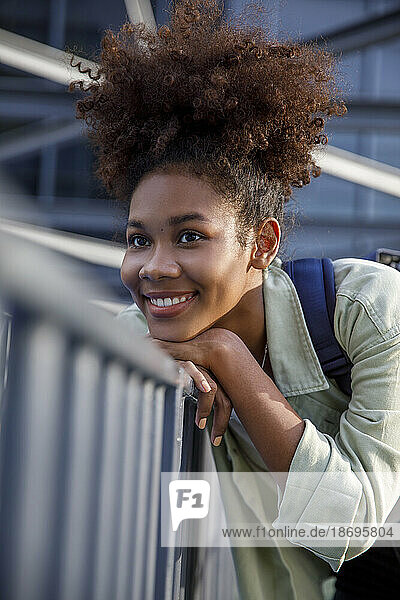 Smiling woman with curly hair contemplating by railing