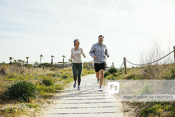 Happy mature couple running on pathway at beach