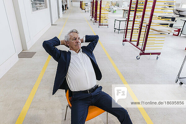Senior businessman with hands behind head sitting on chair in factory