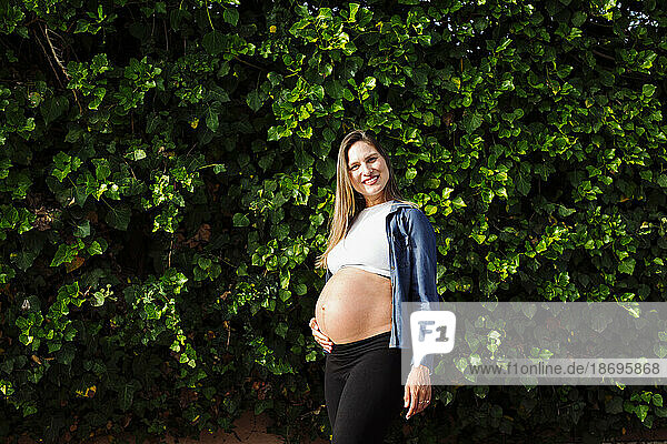 Smiling pregnant woman standing in front of hedge