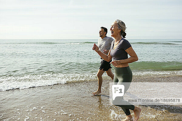 Happy mature couple laughing and running in water at beach