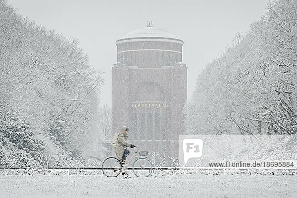 Germany  Hamburg  Person riding bicycle past Stadpark planetarium during heavy snowfall