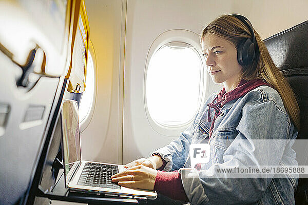 Young woman using laptop and listening music in airplane