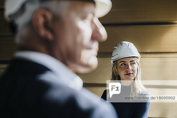Businesswoman wearing hard hat with businessman in factory