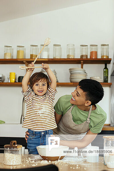 Happy woman with son holding ladles in kitchen at home