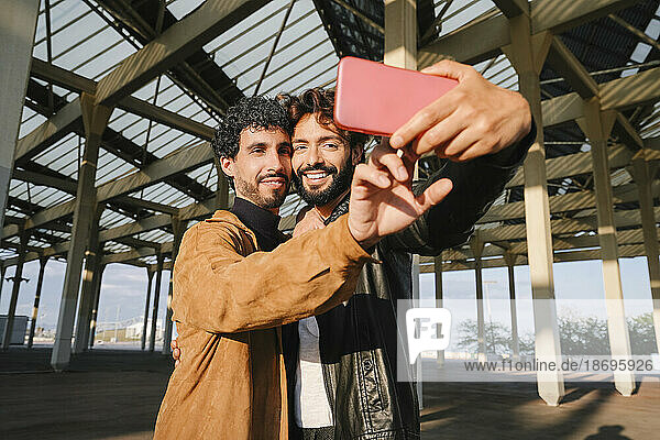 Gay men taking selfie through smart phone under concrete structure