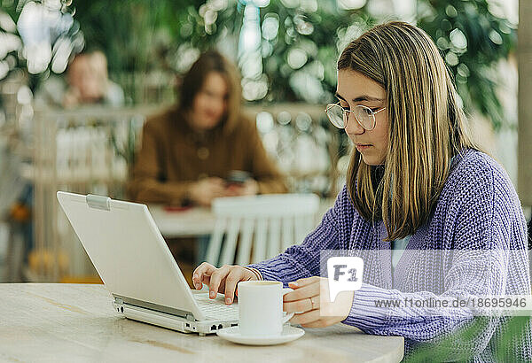 Girl holding coffee cup using laptop sitting at school cafeteria
