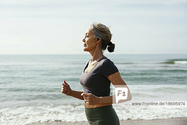 Mature woman with wireless in-ear headphones running at beach