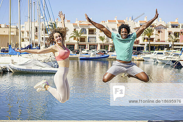 Happy couple jumping with arms raised on pier at harbour