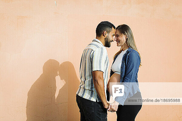 Glückliche schwangere Frau steht mit Mann vor der Wand
