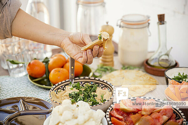 Hand hält Hummus  umgeben von gesunder Mahlzeit in Schüsseln und veganem Produkt