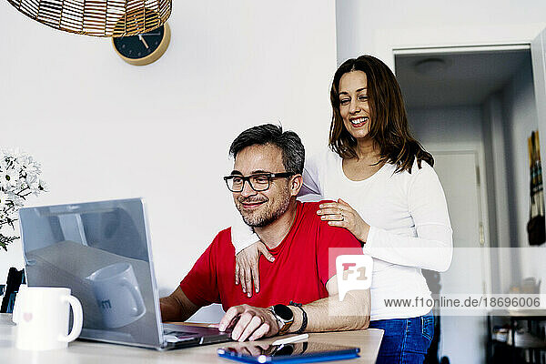 Woman with arm around man working on laptop at home