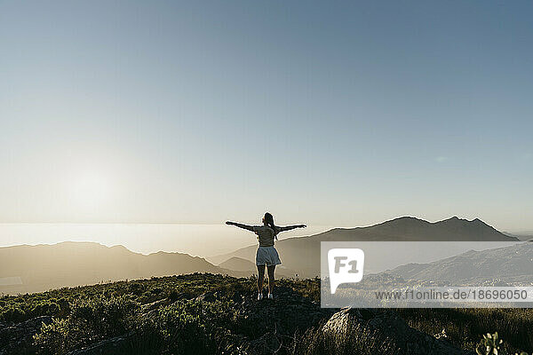 Woman with arms outstretched standing on mountain under sky