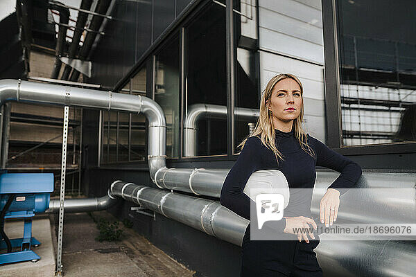 Businesswoman leaning on metal pipes at factory