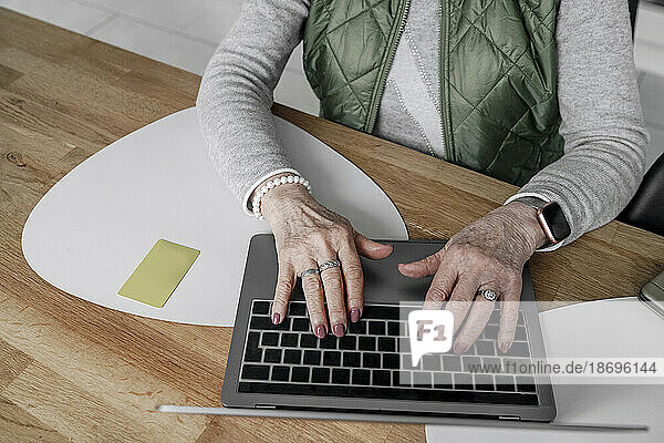 Hände einer älteren Frau  die zu Hause über den Laptop online einkauft