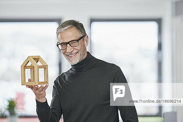 Portrait of smiling senior architect holding model house in office