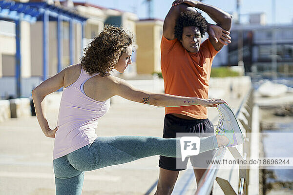 Couple stretching and exercising on pier in coastal area