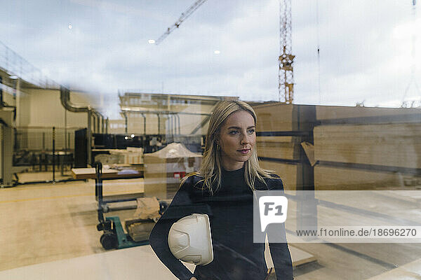 Businesswoman standing in factory seen through glass