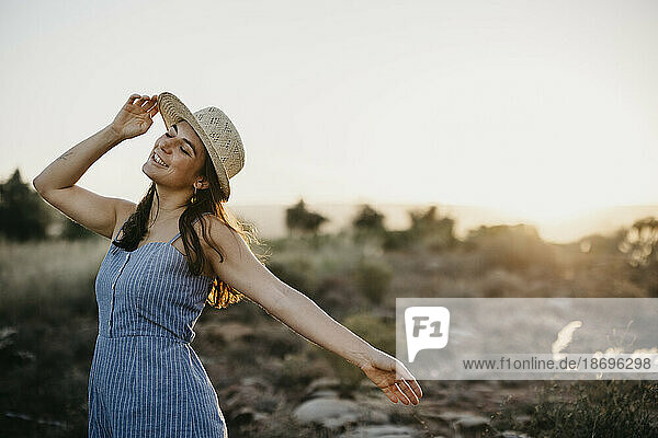 Carefree woman wearing hat dancing in field
