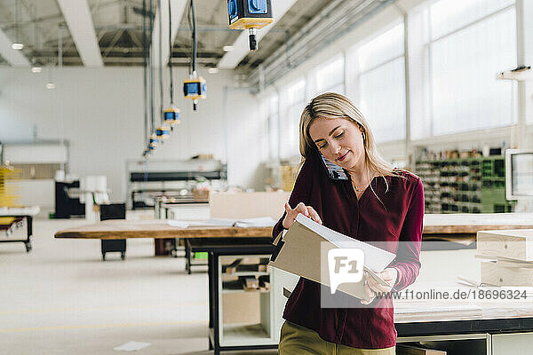 Businesswoman going through documents and talking on smart phone in factory