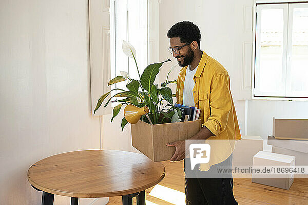 Smiling man holding cardboard box in new apartment
