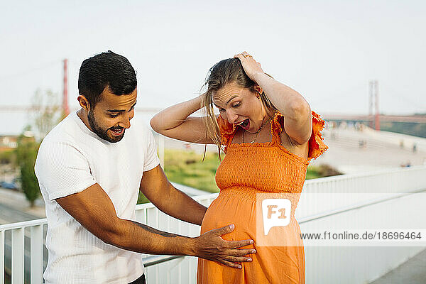 Man touching belly of surprised pregnant woman