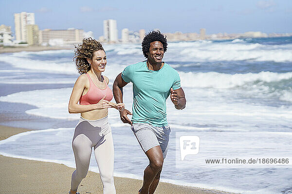 Happy couple wearing sportswear running at seashore