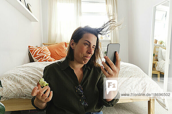Woman blowing hair and taking selfie through smart phone at home