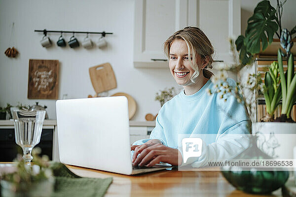 Smiling woman using laptop on dining table at home
