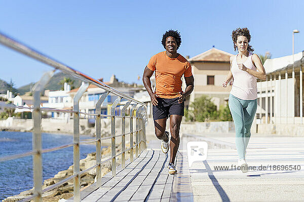 Couple running by pier near sea in coastal area