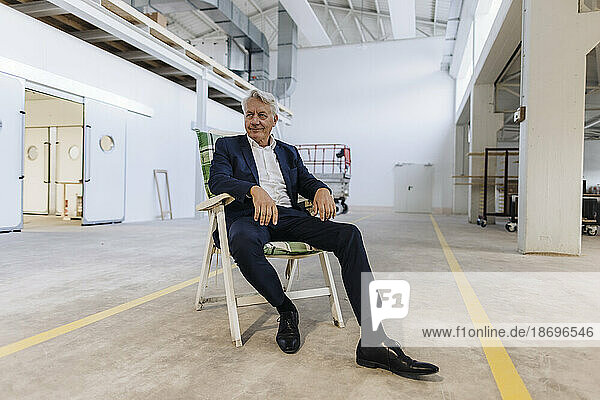 Senior businessman resting on chair in factory