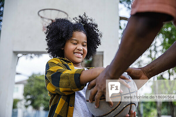 Smiling girl taking basketball form father at sports court