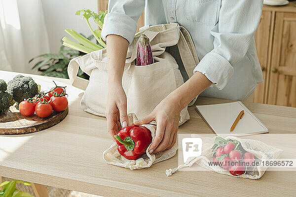 Woman keeping vegetables in reusable bags on table at home