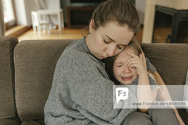Mother consoling crying daughter on sofa