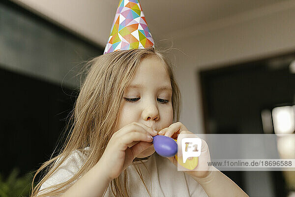 Girl wearing party hat inflating balloon at home