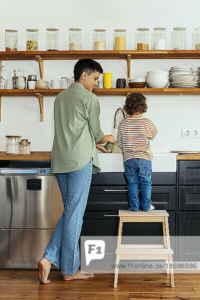 Woman doing dishes with son in kitchen at home