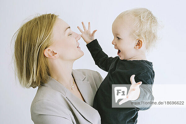 Playful son with mother against white background