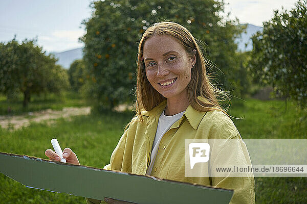 Lächelnde Frau mit ausgeschnittenem Karton und Filzstift im Garten