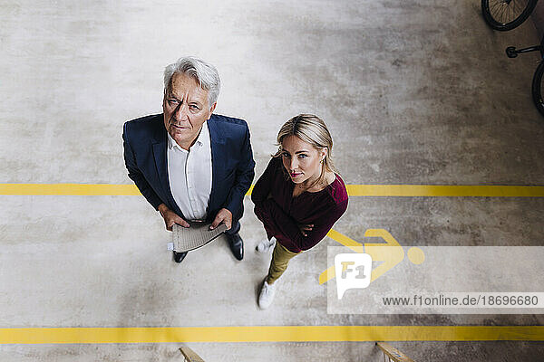 Confident businesswoman and senior businessman standing on floor in factory