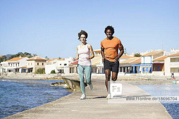 Couple running on pier near sea in coastal area