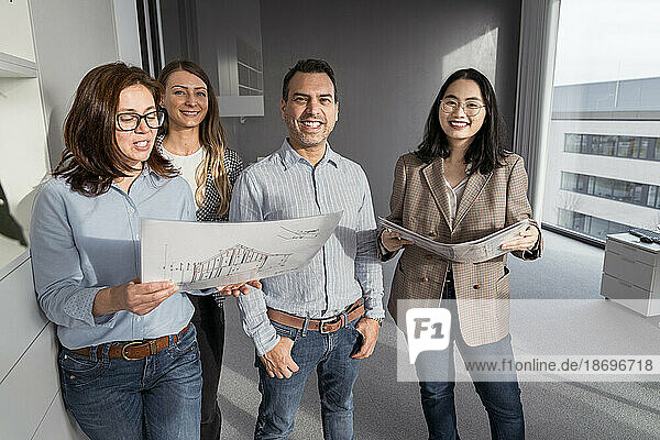 Confident business people standing in office holding architectural plans