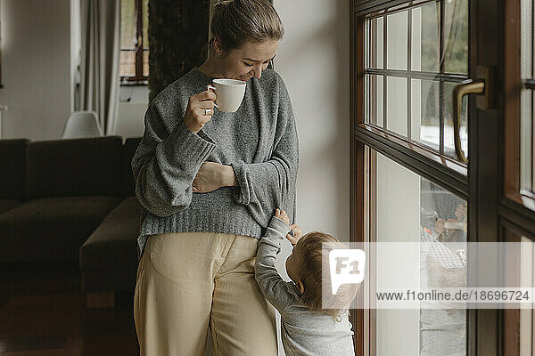 Son standing with mother holding coffee cup at home
