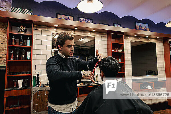 Barber cutting hair of customer sitting in shop