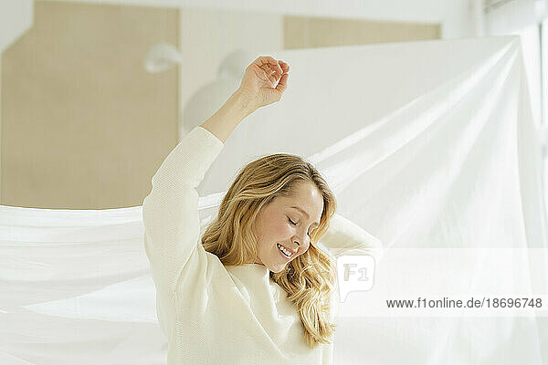 Smiling woman with arms raised by curtain