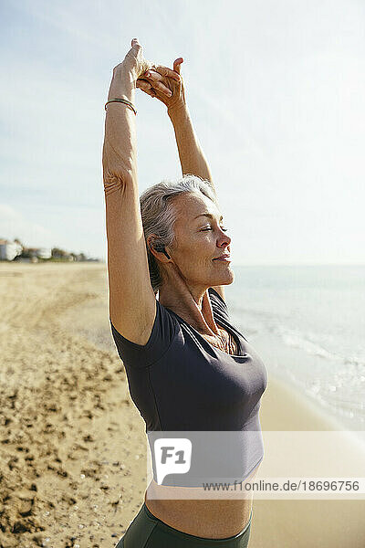 Mature woman stretching with eyes closed at beach