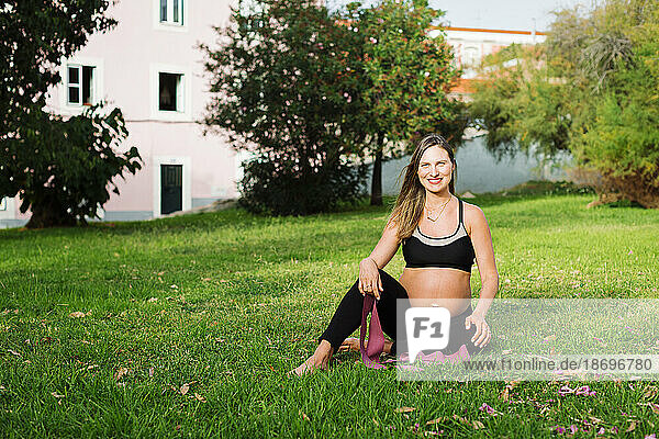 Smiling pregnant woman with resistance band sitting on lawn