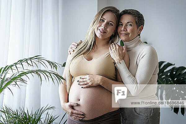 Lächelnde ältere Frau umarmt schwangere Tochter  die zu Hause steht