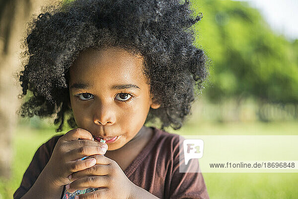 Boy with curly hair sipping drink through straw at park