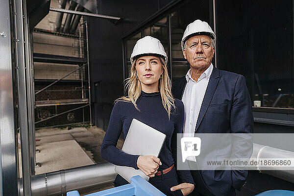 Confident businessman with colleague holding laptop at factory