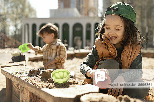 Lächelnder Junge  der an einem sonnigen Tag mit Sand auf dem Spielplatz spielt